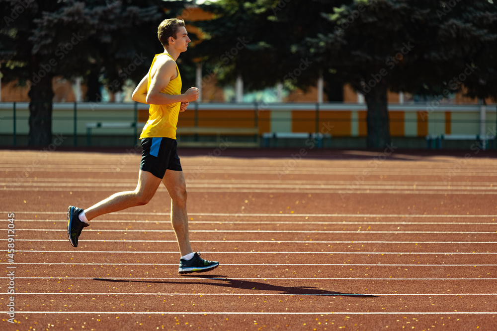Young Caucasian sportive man, male athlete, runner jogging at public stadium, sport court or running track outdoors. Summer sport games.