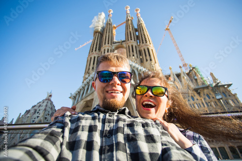 Happy tourists photographing in front of the famous Sagrada Familia roman catholic church in Barcelona, architect Antoni Gaudi