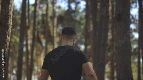 Young man wearing a black t-shirt, walking through the forest, back view.  Male traveler with walks along forest rear view, leisure, bio-tourism, Hiking. 