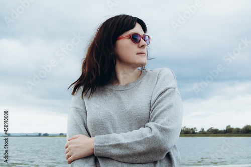 Young woman in glasses on the shore looks with a smile to the side. Concept calmness and solitude