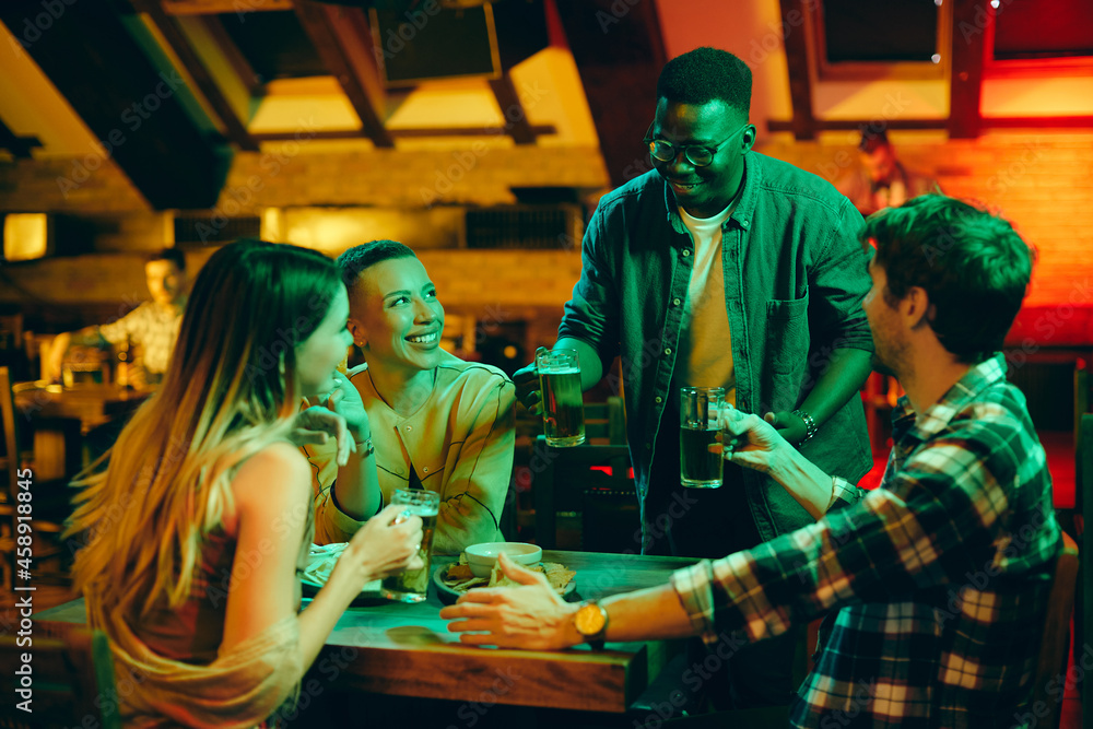 Happy African American man having fun while drinking beer with his friends i a pub.