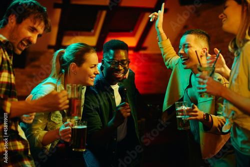 Group of cheerful friends singing karaoke during their night out in a bar.