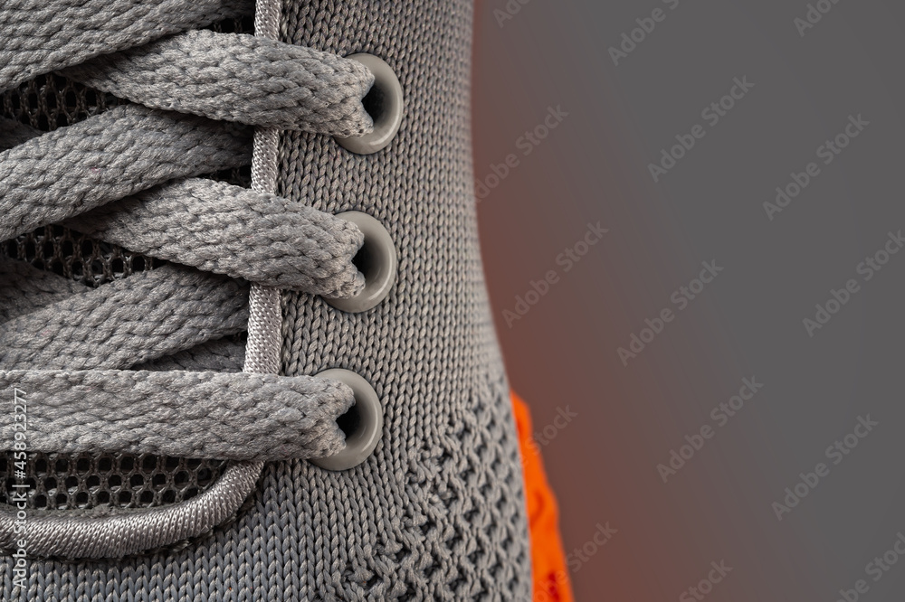 Laced up gray mesh fabric sneakers macro shot. Laced fastening of new orange sole sport shoe close-up. Elastic laces of modern textile trainers for active lifestyle, sport and fitness. Copy space. - obrazy, fototapety, plakaty 