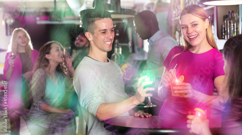 Cheerful young man flirting with women on party and drinking cocktails at nightclub