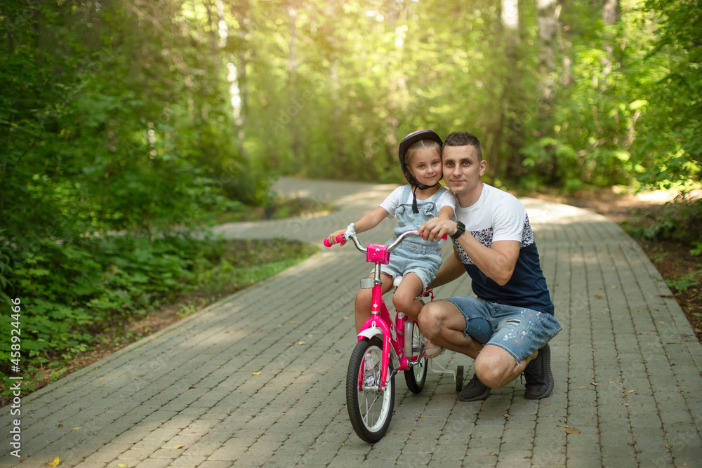 Happy father teaching his little daughter to ride a bicycle. Child learning to ride a bike. Family activities at summer. Happy father teaching his little daughter to ride a bicycle. Child learning to ride a bike. Family activities at summer.