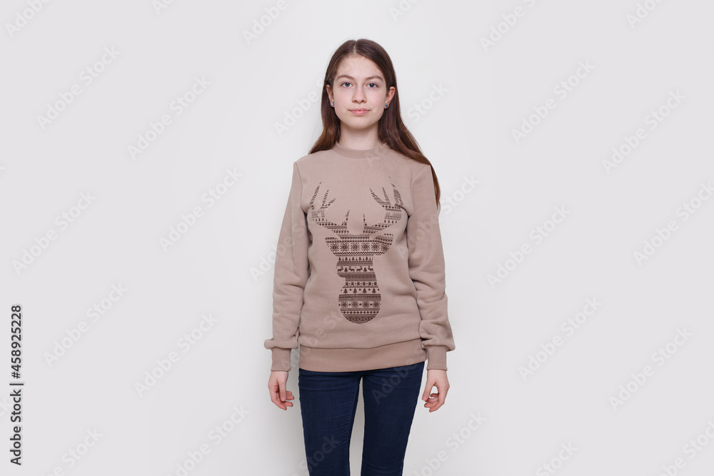 Front portrait of a beautiful unhappy teenage girl in a sweater, staring at the room, standing on a white background. Front portrait of a beautiful unhappy teenage girl in a sweater, staring at the room, standing on a white background.