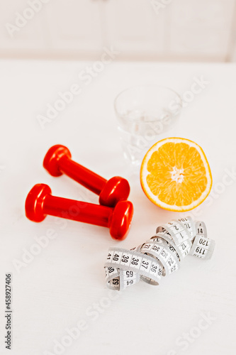 A centimeter, an orange, a glass of water and red dumbbells. Health care, diet and sport concept