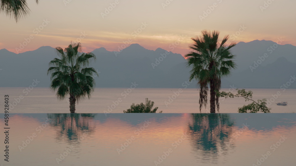 Resort scene at sunset Swimming pool with palms, sea and mountains