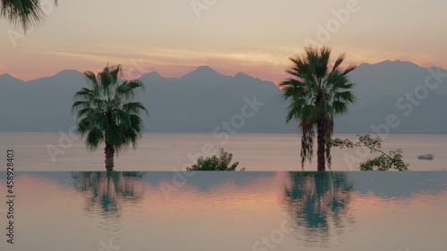 Resort scene at sunset Swimming pool with palms, sea and mountains
