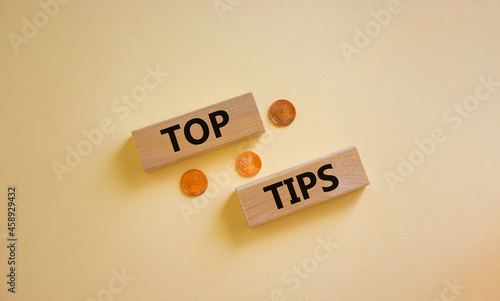 Top tips symbol. Concept words 'top tips' on wooden blocks on a beautiful white background, metallic coins. Business and top tips concept, copy space.