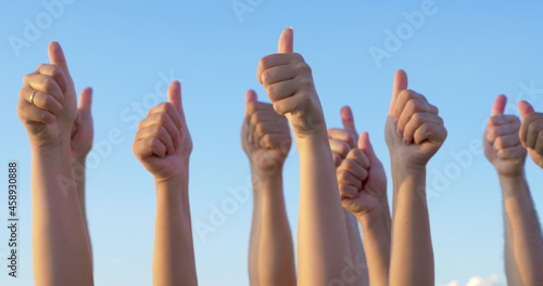 Hands with thumbs up raised against blue sky