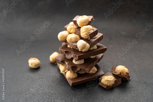 milk chocolates bars with nuts on black table. Hazelnut milk chocolate pieces tower close up. Sweet food photo concept. Chunks of broken chocolate. Confectionery craft for chocolate background