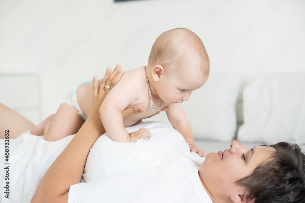 Happy smiling mother and baby lying on bed at home Happy smiling mother and baby lying on bed at home