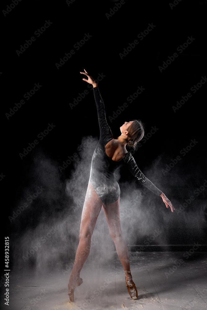Art perfomance. Full-length portrait of talented flexible dancer moving in cloud of dust, female dancer in flour. Isolated over black studio background. Dance, people, art, performance concept