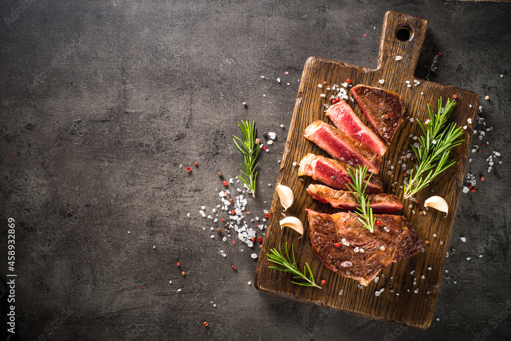 Grilled Beef steak at wooden cutting board with spices. Top view with copy space at black background. Grilled Beef steak at wooden cutting board with spices. Top view with copy space at black background.