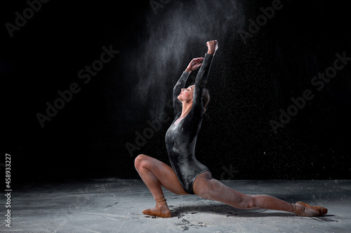 Attractive Caucasian Woman In Black Bodysuit Is Moving Gracefully, In Black Studio With Flour, Athlete Female Is Flexible And Elegant, Make Performance Alone. Art, Dance Concept