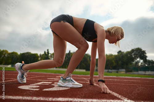 Side view of motivated young female athlete ready to run at track field in the daytime
