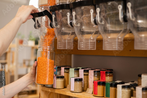 A man fills a jar with red lentils. Selling bulk goods by weight in an eco store. Trade concept without plastic packaging