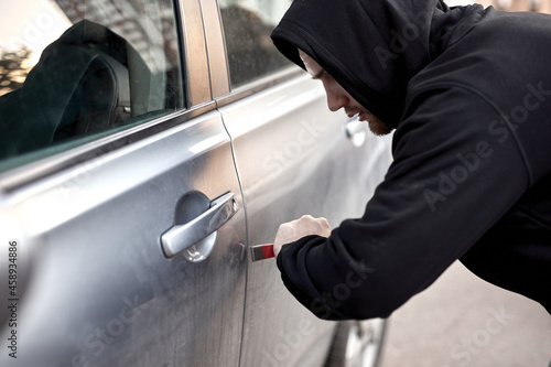 Unrecognizable Car thief steal car breaking door criminal job burglar Hijacks Auto thief is trying break into automobile using tools. Street crime violence gangster robber automobile parking