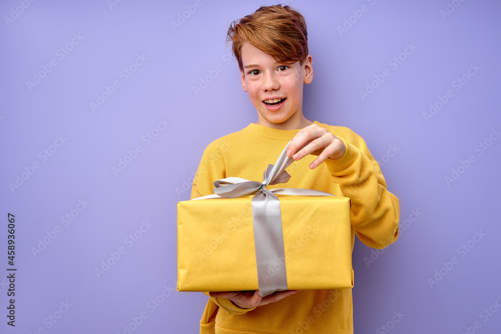 Amazed curious adorable little boy unpacking present box with funny astonished expression, impatient caucasian child in yellow wear unboxing birthday surprise. studio shot purple background. Amazed curious adorable little boy unpacking present box with funny astonished expression, impatient caucasian child in yellow wear unboxing birthday surprise. studio shot purple background.