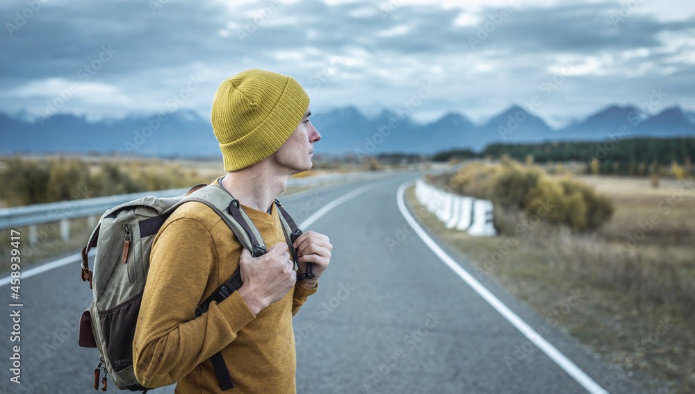 Man with a backpack on a road, against the background of mountains. Concept of freedom, autumn, travel and hiking Man with a backpack on a road, against the background of mountains. Concept of freedom, autumn, travel and hiking
