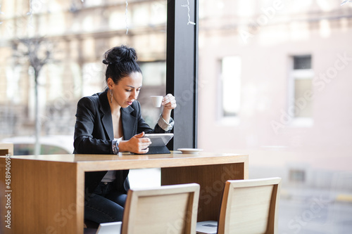 Businesswoman at a cafe, having coffee and looking at tablet.