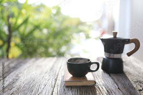 Black coffee cup and black moka pot with leather notebook on wooden table