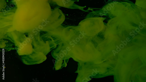 Green cloud of ink. Awesome abstract background. Drops of green ink in water. Cosmic star background. Green watercolor paints in water on a black background.