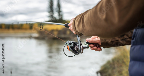 Male fisherman is fishing in a quiet place on the river in the autumn forest. Closeup