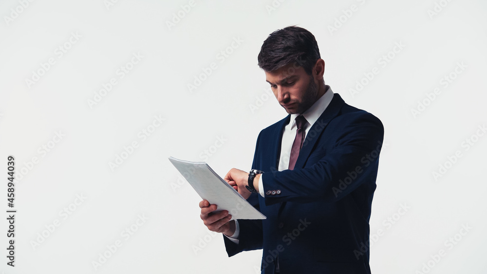 Businessman looking at wristwatch while holding papers isolated on white Businessman looking at wristwatch while holding papers isolated on white