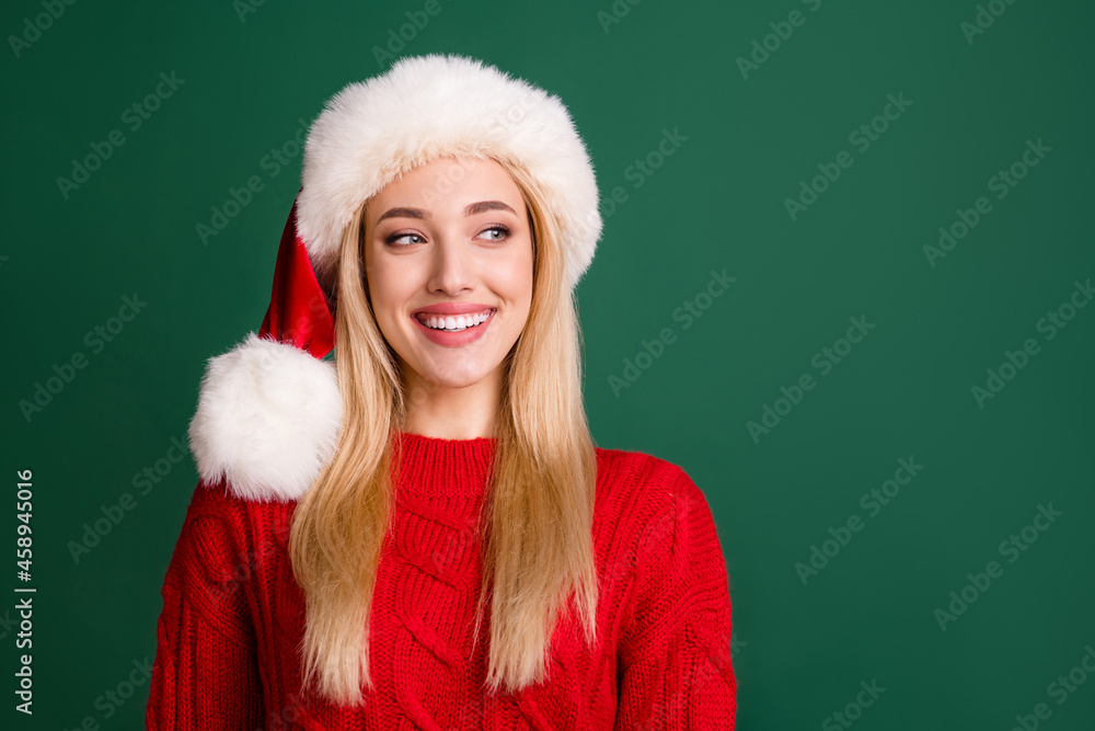 Photo of pretty nice positive woman look empty space wear santa claus hat smile isolated on green color background Photo of pretty nice positive woman look empty space wear santa claus hat smile isolated on green color background