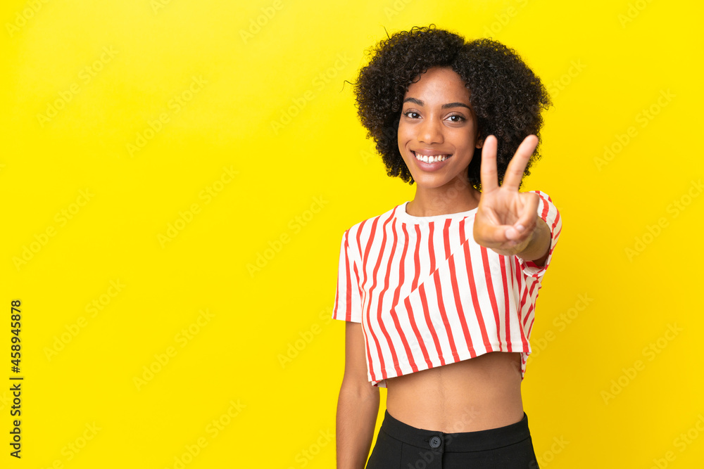 Young African American woman isolated on yellow background smiling and showing victory sign