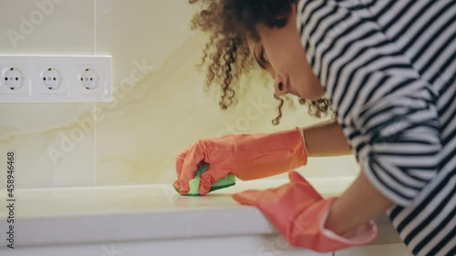 Young housewife cleaning dirty surface in kitchen with sponge, perfectionism photo