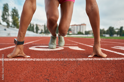 Close up shot of strong arms and legs of professional young female runner ready to race on track field at stadium