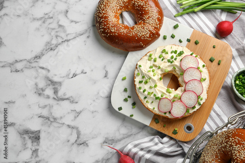 Delicious bagel with cream cheese, green onion and radish on white marble table, flat lay. Space for text