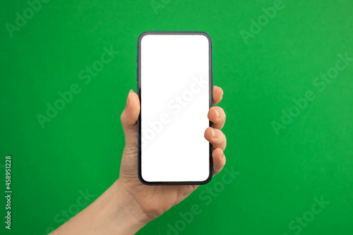Hand with mobile phone mockup screen on a green background, copy space photo