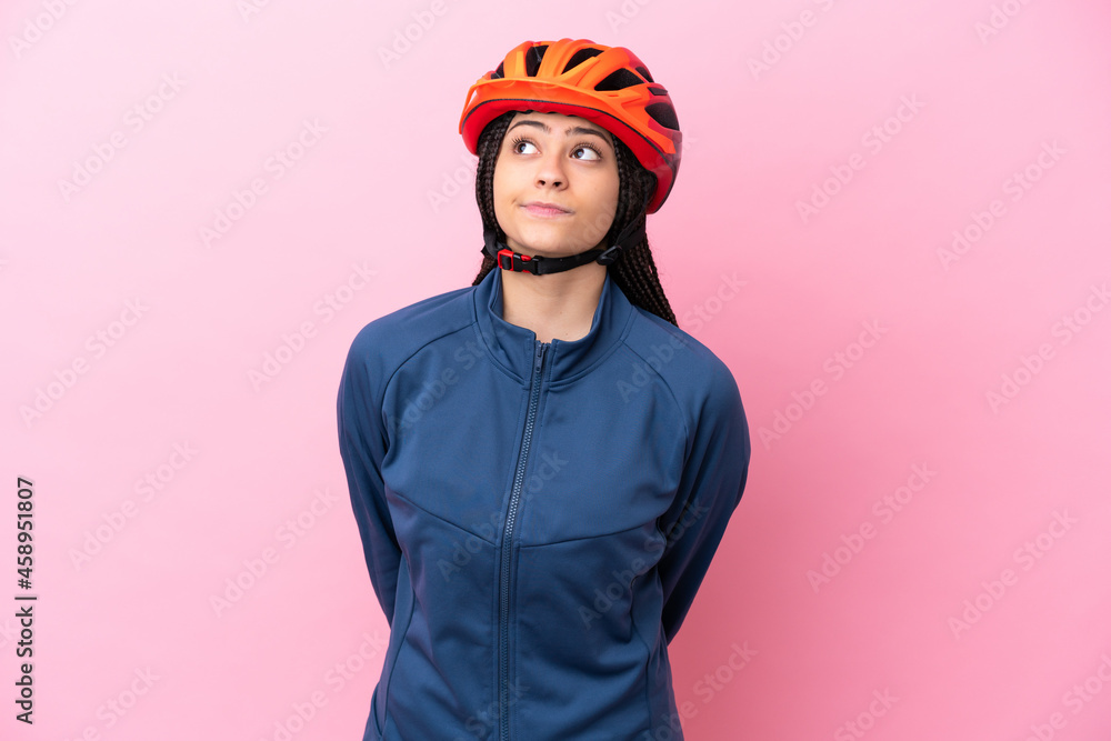 Teenager cyclist girl isolated on pink background and looking up - obrazy, fototapety, plakaty 