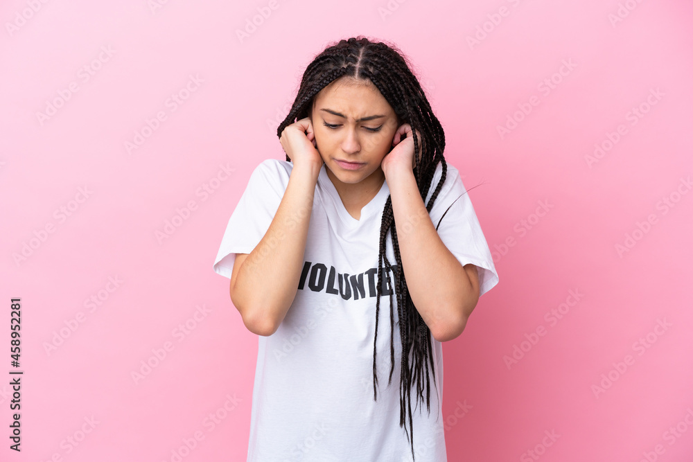 Teenager volunteer girl with braids isolated on pink background frustrated and covering ears Teenager volunteer girl with braids isolated on pink background frustrated and covering ears