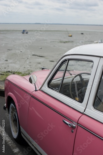 side of a vintage pink car parked in front of a beach