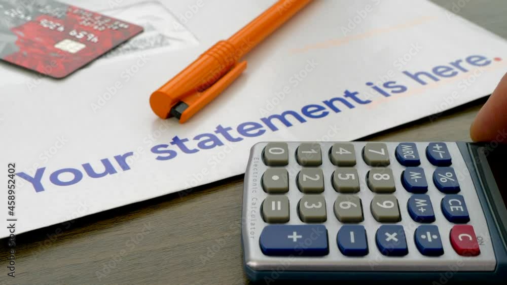 Closeup POV shot of a customer letter bearing the words ‘Your statement is here’, with a defocused plastic bank card and a pen on top, then a sharply focused calculator being slid into the frame. Closeup POV shot of a customer letter bearing the words ‘Your statement is here’, with a defocused plastic bank card and a pen on top, then a sharply focused calculator being slid into the frame.