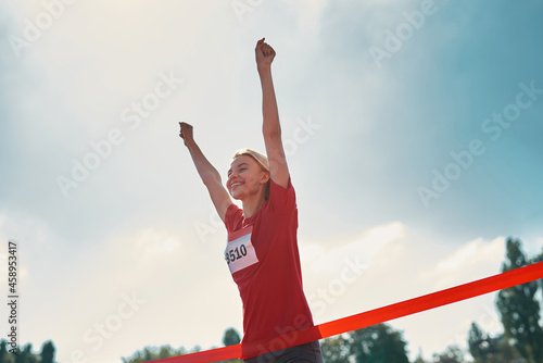 Low angle view of excited young female athlete with arms raised reaching the finish line at track field during marathon outdoors
