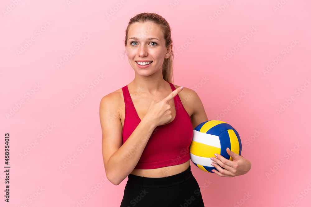 Young caucasian woman playing volleyball isolated on pink background pointing to the side to present a product