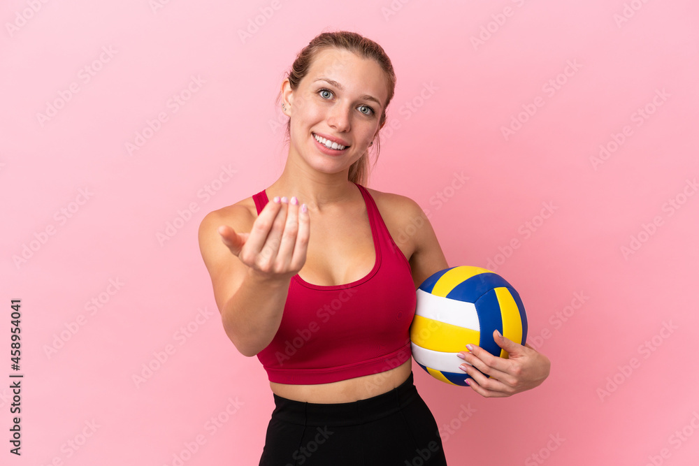 Young caucasian woman playing volleyball isolated on pink background inviting to come with hand. Happy that you came