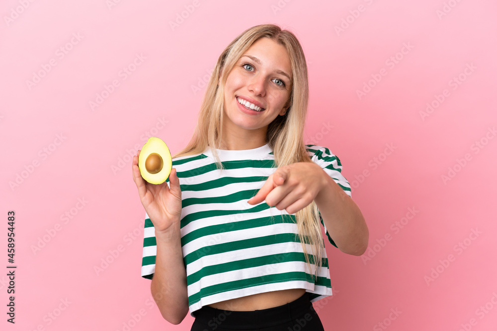 Young caucasian woman holding an avocado isolated on pink background pointing front with happy expression Young caucasian woman holding an avocado isolated on pink background pointing front with happy expression