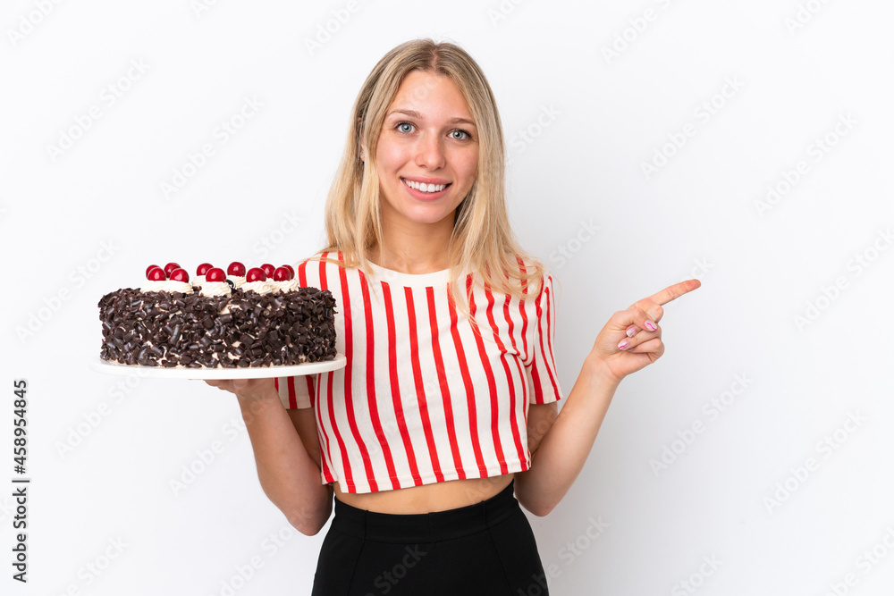 Young caucasian woman holding birthday cake isolated on white background pointing finger to the side Young caucasian woman holding birthday cake isolated on white background pointing finger to the side