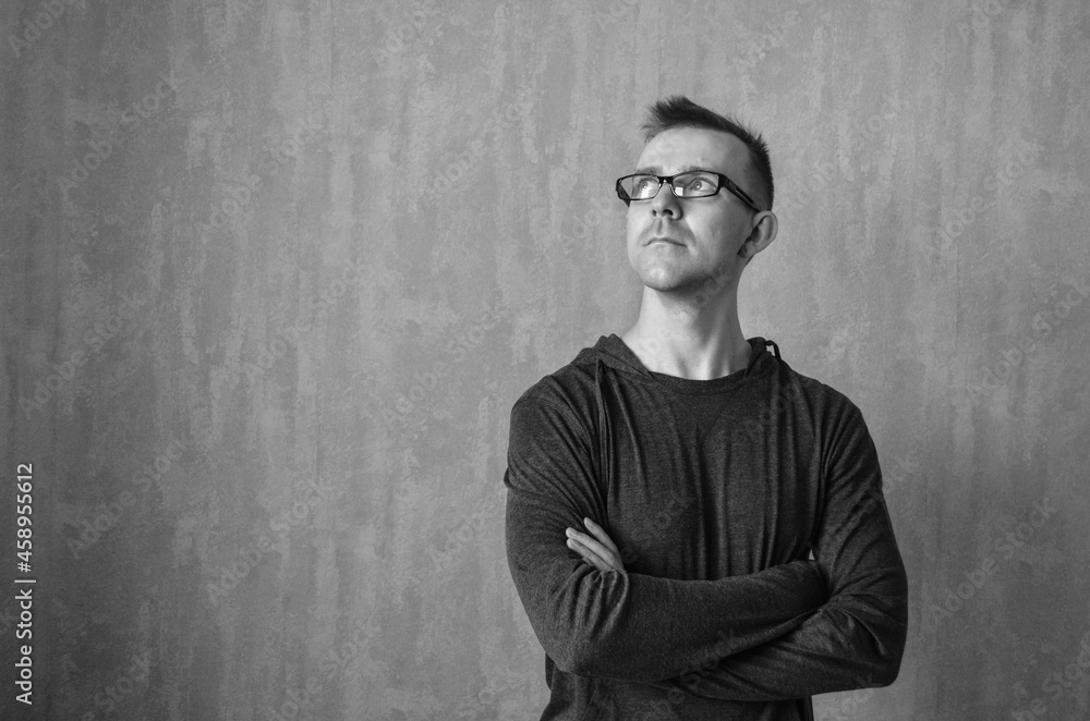 Caucasian man in glasses looking up and standing with folded arms on gray background. Monochrome portrait of pondered or dreamed male with copy space. Thinking concept. Caucasian man in glasses looking up and standing with folded arms on gray background. Monochrome portrait of pondered or dreamed male with copy space. Thinking concept.