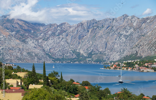 Picturesque panoramic view of the Bay of Kotor and the old town of Kotor at the foot of the high mountain Pestingrad. White pleasure sailing yachts sail across the bay