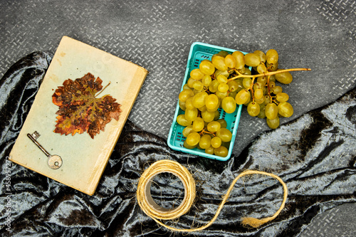 fresh green and yellow grape on basket, old book and key, maple leaf, hello November and autumn concept 