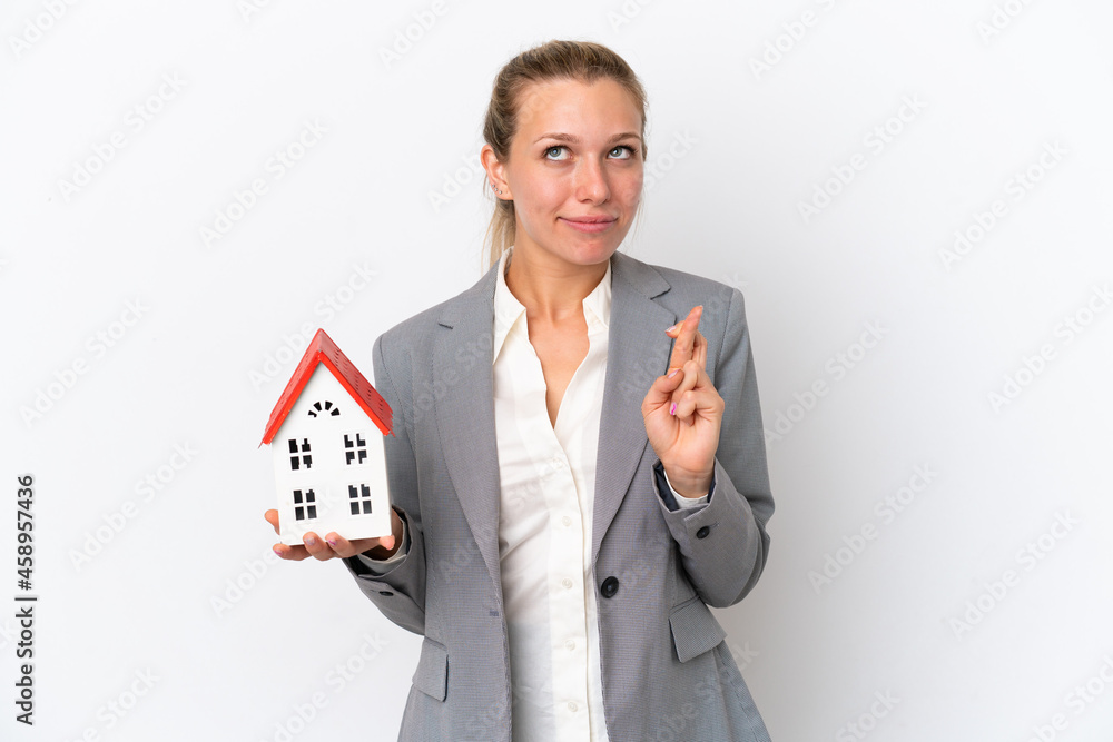 Real estate agent woman holding a toy house isolated on white background with fingers crossing and wishing the best Real estate agent woman holding a toy house isolated on white background with fingers crossing and wishing the best