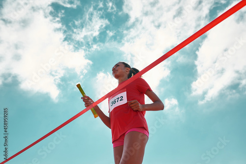Low angle view of female young athlete with baton reaching the finish line at track field during relay competition outdoors